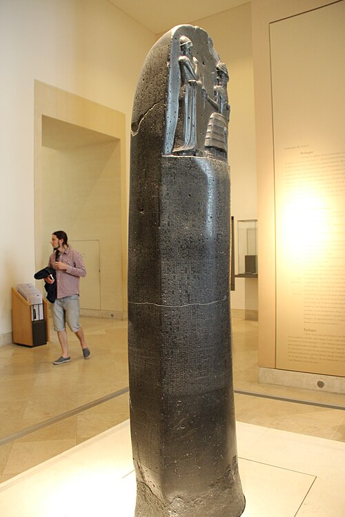 Tall dark stone stele of Hammurabi in the Louvre, with two carved figures above rows of cuneiform writing.