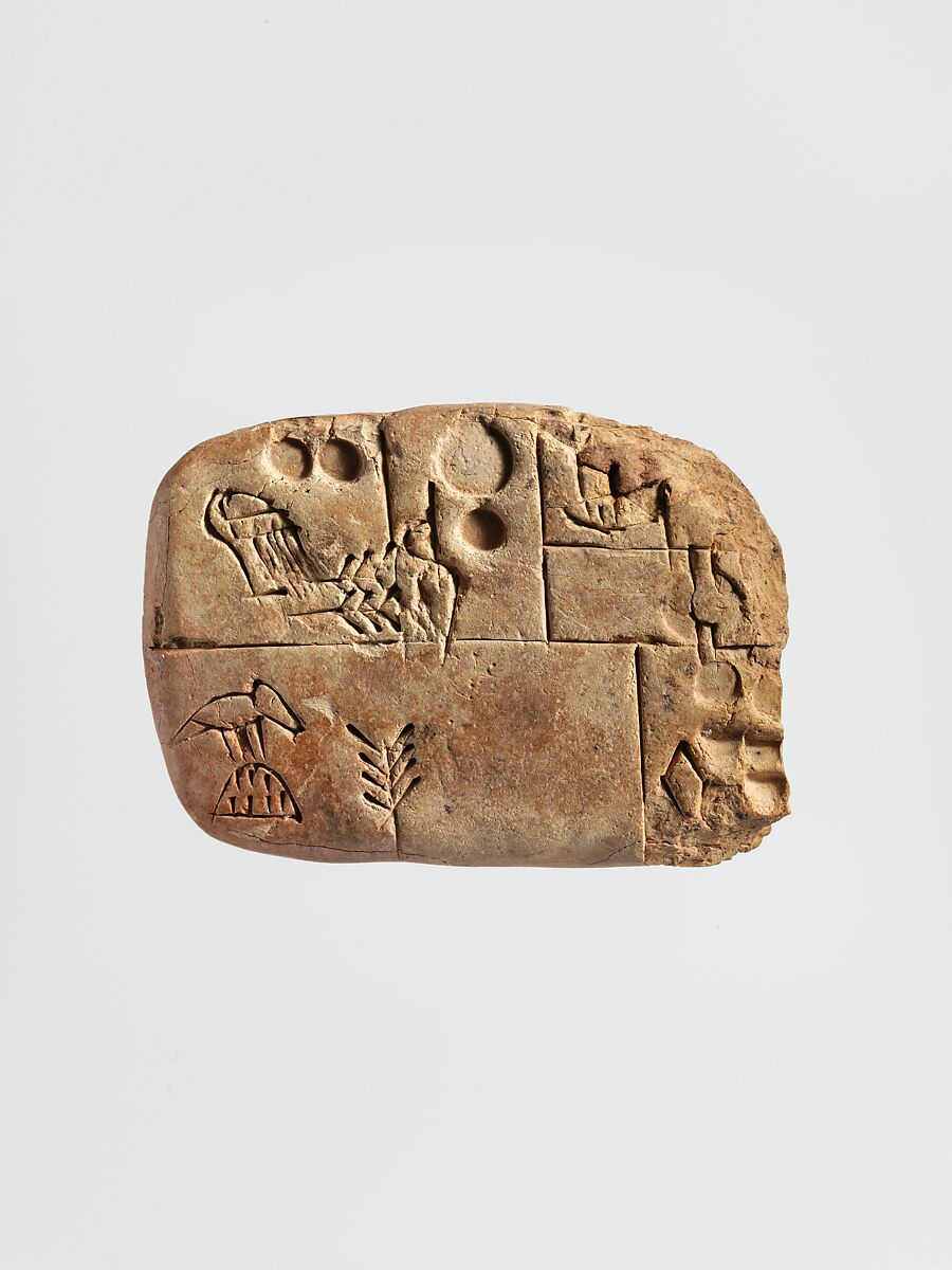 Small tan clay tablet with incised lines dividing its face into sections containing circular impressions and other marks.