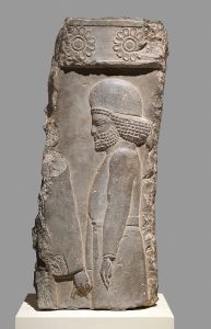 Limestone relief from Persepolis showing a Median man in a belted tunic and rounded cap, holding the hand of a figure ahead of him.
