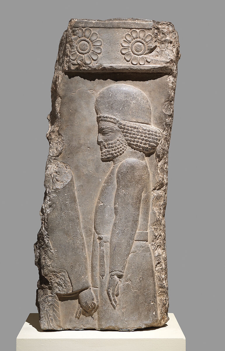 Limestone relief from Persepolis showing a Median man in a belted tunic and rounded cap, holding the hand of a figure ahead of him.